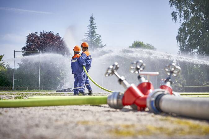 Verteiler bei einem Löschangriff. Im Hintergrund ein Trupp der Jugendfeuerwehr bei der Wasserabgabe